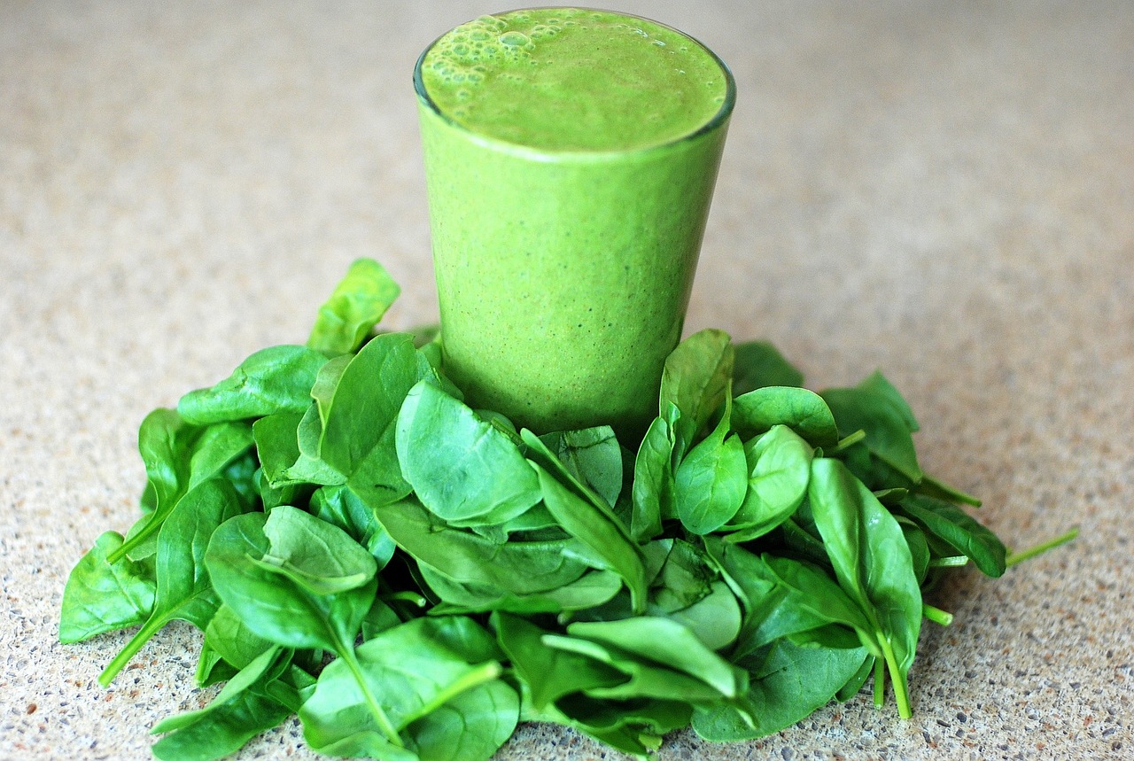 a glass of bright green nutrient packed juice on a table covered with leafy greens